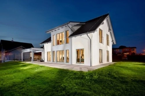 Moderní luxusní dům s osvětlenými okny na pozadí večerního nebe.