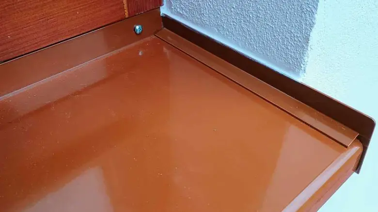 Hladký hnědý vnitřní parapet u bílé zdi.
