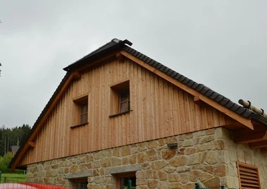 Dům s provětrávanou fasádou z dřevěného obkladu nad kamenným základem.