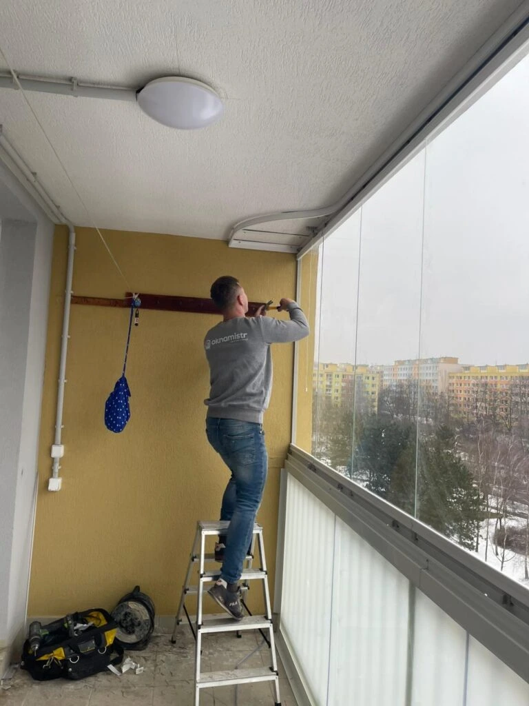 Muž instaluje skleněné panely na balkon pro jeho zasklení.