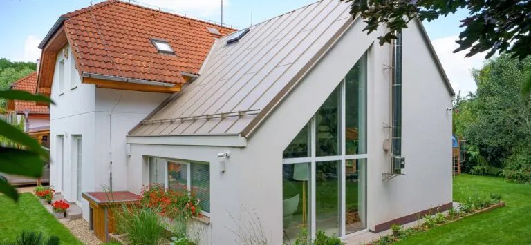 Moderní dům s výraznou kovovou štítovou střechou v zahradě.