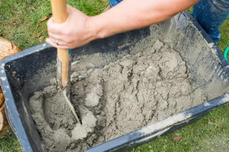Člověk míchá beton lopatou v vozíku na trávníku.