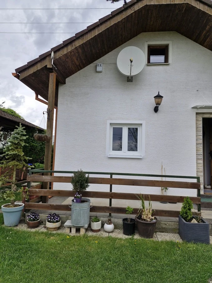 Bílá fasáda s oknem ve štítu a satelitní anténou.