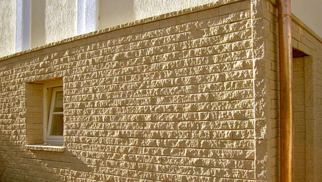 Texturovaný obklad zvenku domu s oknem ukazuje použití materiálu ve stavbě.