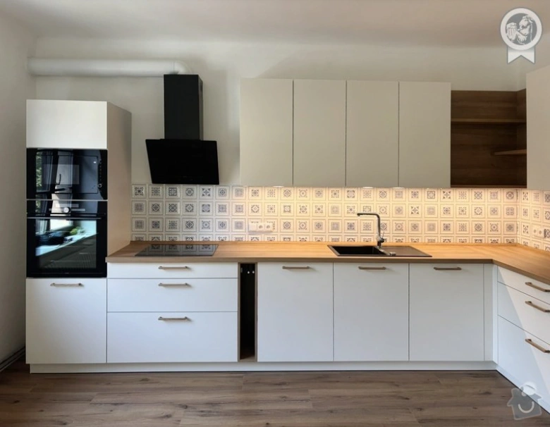 Moderní kuchyně na míru s bílými skříněmi a dřevěnou pracovní deskou.