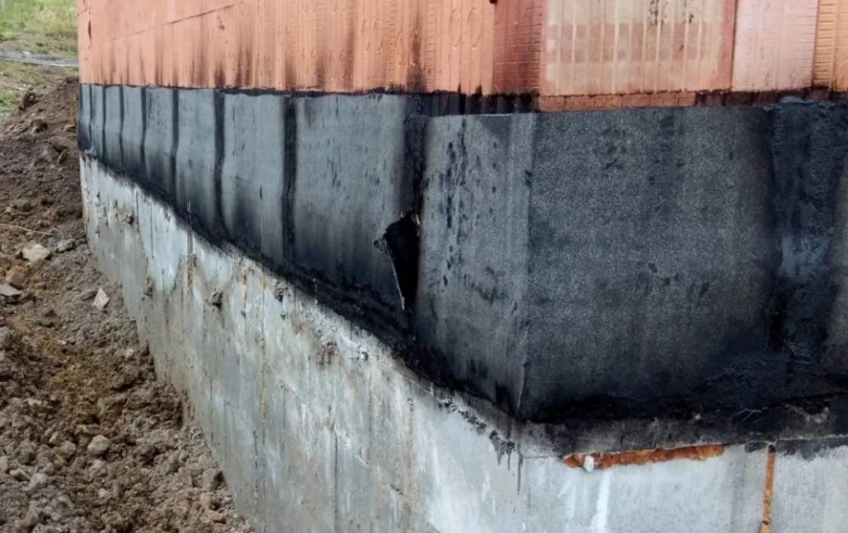 Detail hydroizolace základny s černou membránou na cihlové zdivo.