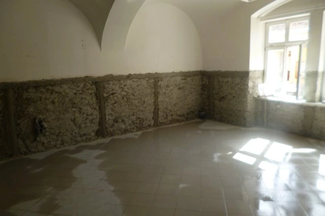 Prázdná místnost s odhalenými zdivovými stěnami po odstranění omítky.