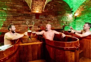 Muži v dřevěných vanách ve wellness prostoru s cihlovými zdmi.