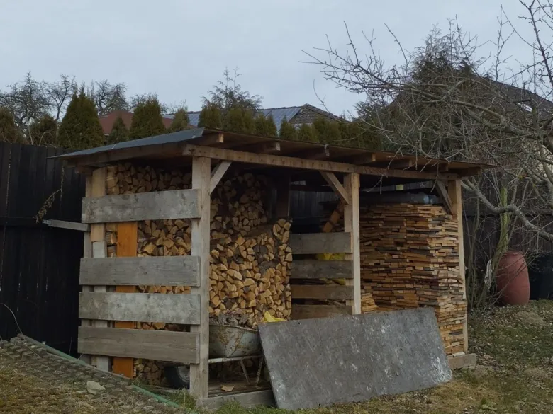 Dřevník postavený z palet s naskládaným dřívím pod přístřeškem.