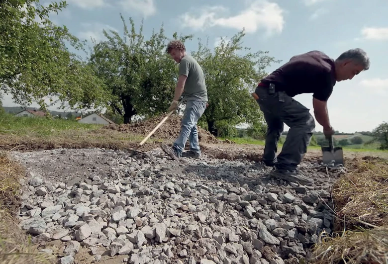 Muži rozkládají štěrkový základ pro betonování domu.