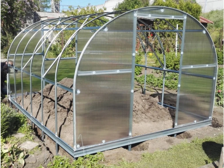 Kovový rám skleníku s polycarbonátovou fólií na zahradě.