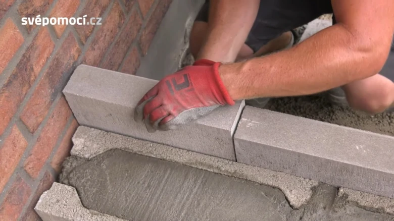 Ruce v rukavicích kladou obrubníky na čerstvý beton.