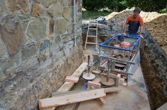 Práce na základové izolaci kamenné zdi s použitím hydroizolačních materiálů.