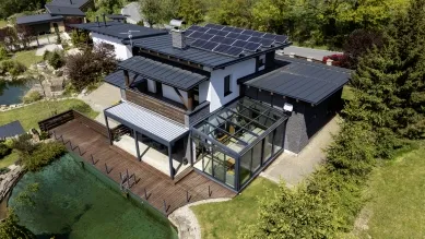 Moderní dům s přistavěnou zimní zahradou na pozadí zelené zahrady.
