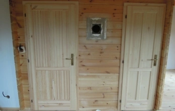Vnitřek dřevěné chaty s dveřmi a větrací otvorem ve zdi.