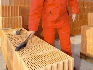 Pracovník v oranžovém oblečení manipuluje s cihlovým materiálem.