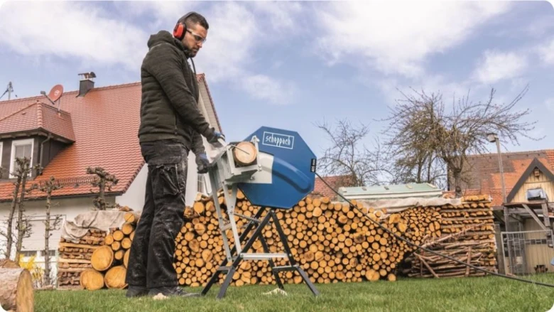 Muž používá pilu na dřevo vedle naskladněného dřeva.