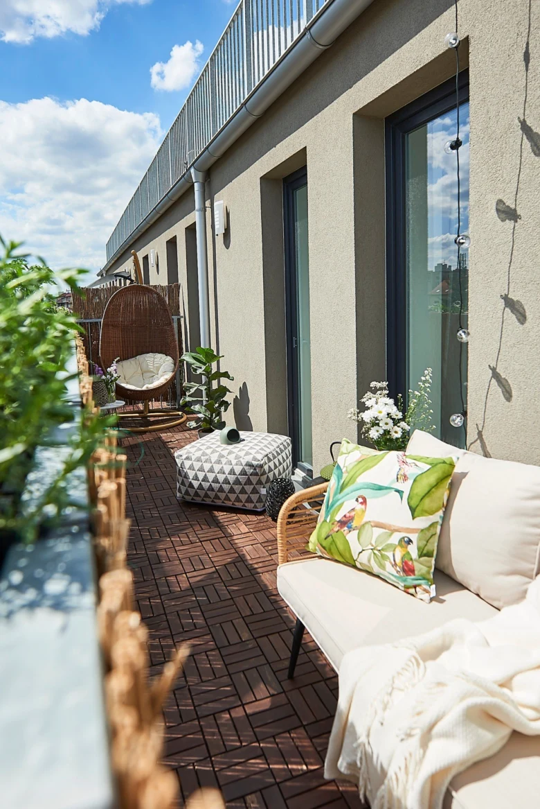 Zelený balkon s gaučem, židlí a rostlinami na slunci.