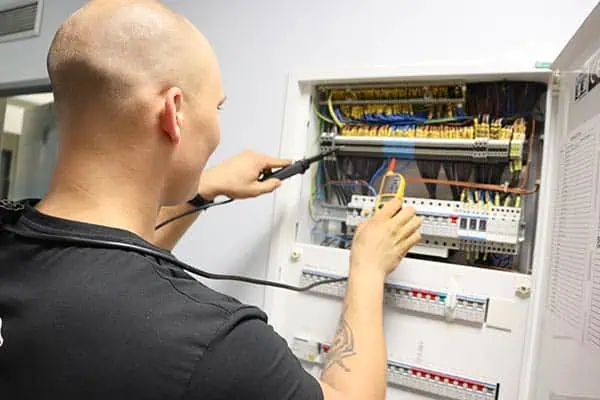 Elektrikář opravuje rozvaděč v domácnosti pomocí měřicího přístroje.
