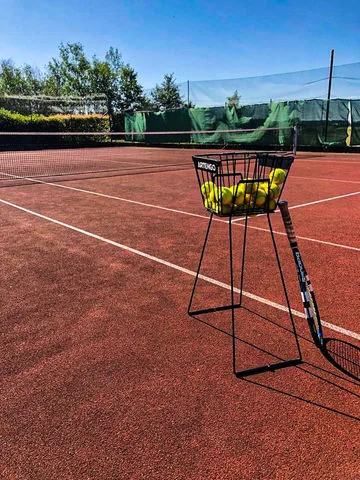 Tennis dvorek s košíkem míčů a raketou na kempu Hracholusky.