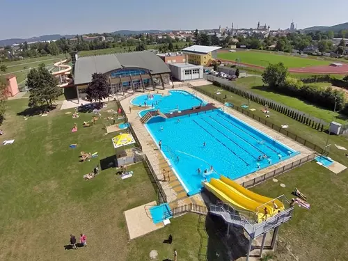 Vzdušný pohled na venkovní bazénový komplex s vodními skluzavkami a soláři.