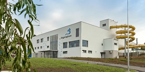 Bílá budova Aquacentrum s žlutými vodními skluzavkami.
