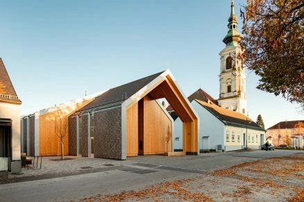 Moderní dřevěná kůlna s kostelem v pozadí na podzimním nádvoří.