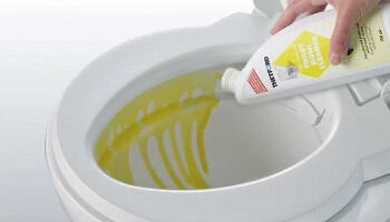 Ruka nalévá žlutý čisticí prostředek do toalety.