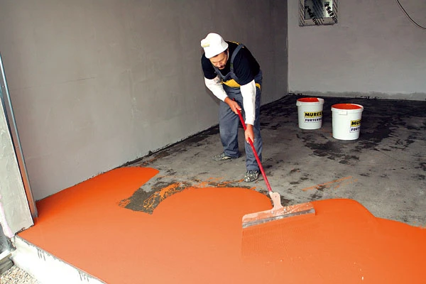 Pracovník nanáší oranžovou epoxi na betonovou podlahu stěrkou.