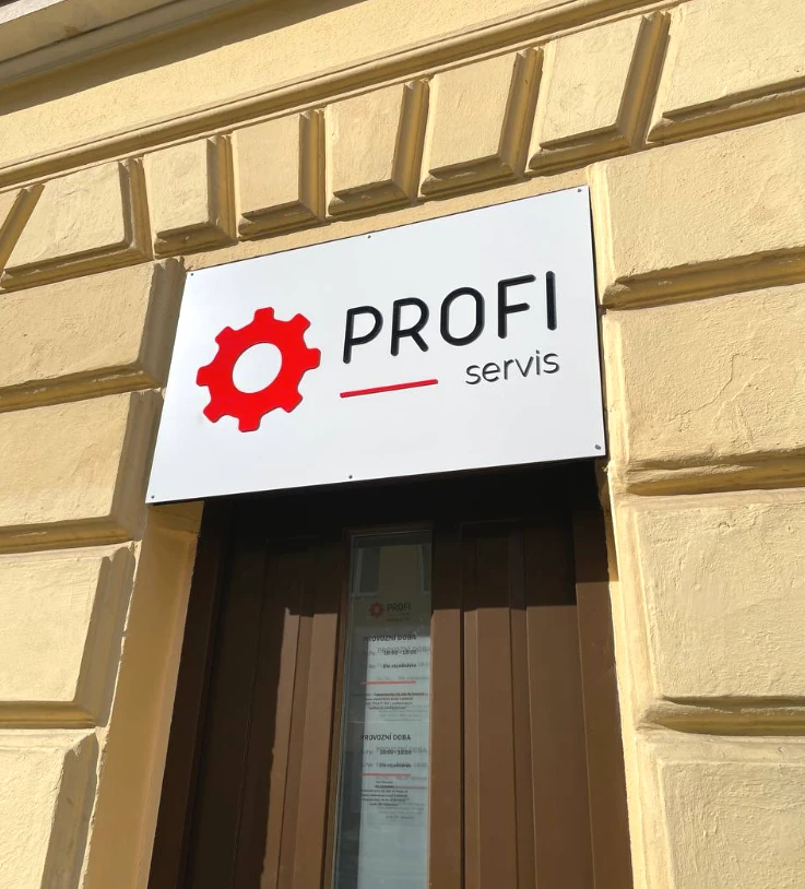Bílá tabule s logem PROFI servis na žluté fasádě budovy.