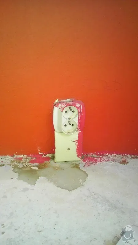 Poškozená elektrická zásuvka na oranžové zdi s vodou pod ní.
