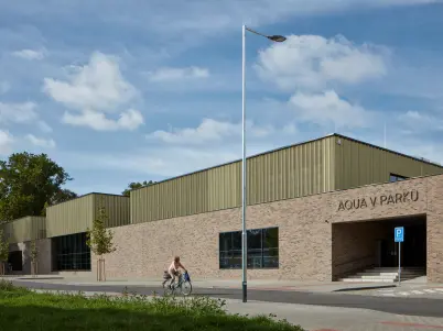 Exteriér bazénu Aquav Parku v Kyjově s cyklisty u vstupu.