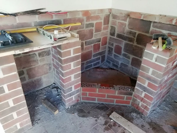 Stavba venkovního krbu z cihel s nástroji na místě.