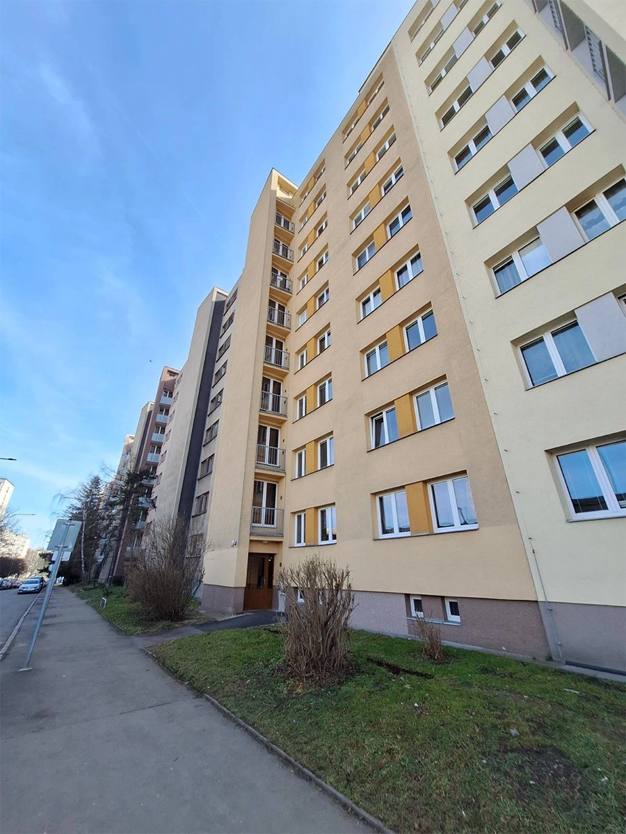 Žlutá fasáda bytového domu s okny na chodníku.