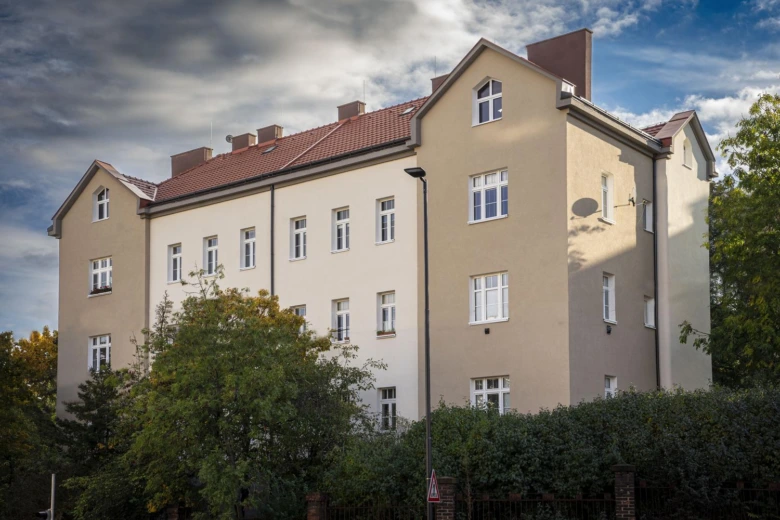 Renovovaná fasáda bytového domu s novými okny a červenou střechou.