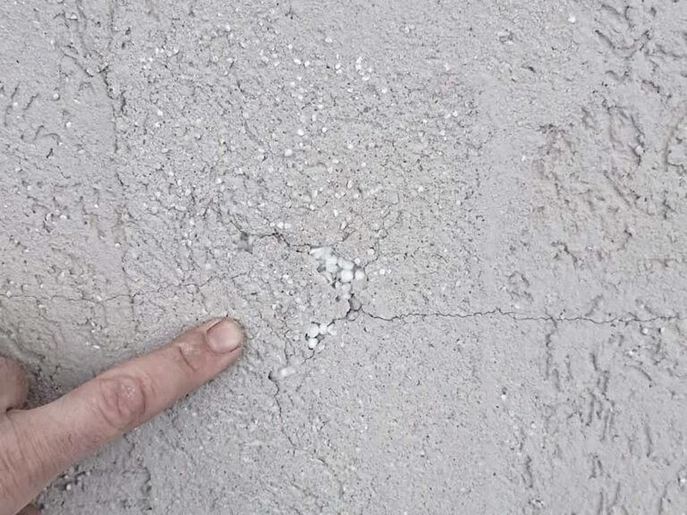 Prasklina na zateplené fasádě ukazovaná prstem