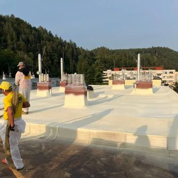 Pracovníci nanášejí PUR pěnu na střechu budovy.