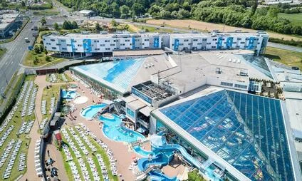 Vzduchový pohled na bazénové centrum s vnitřními a venkovními plavárenskými místnostmi.
