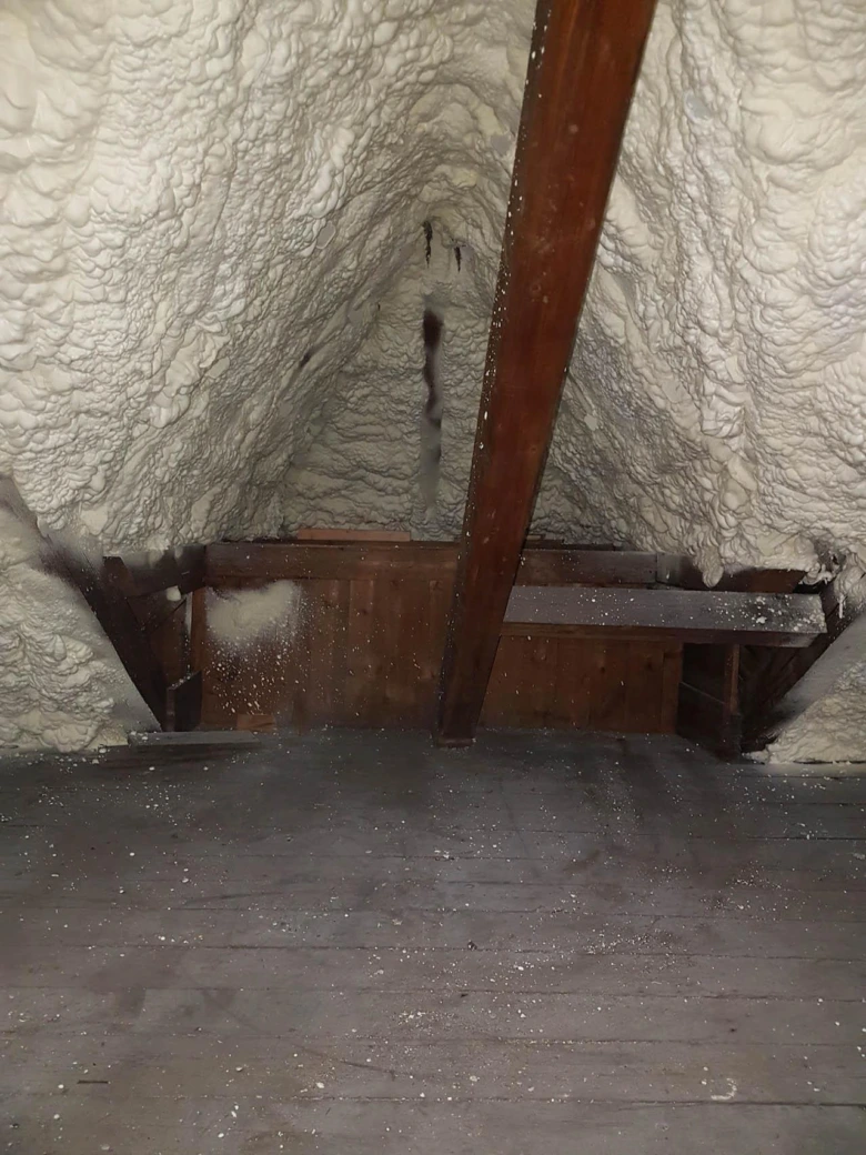 Podkroví zateplené pěnovou izolací s dřevěnými trámy a nosníky.