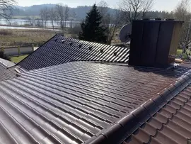 Plechová střešní krytina s komínem na pozadí krajiny.